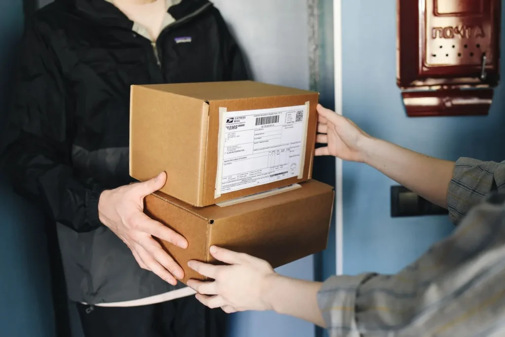 A person in black and gray jacket handing over boxes to a person